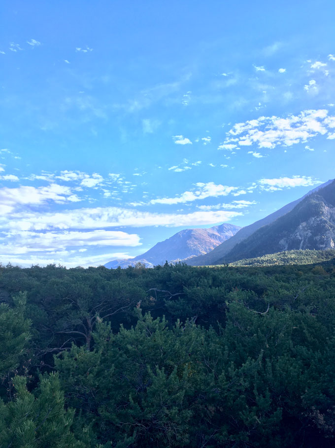 Un paysage de montagne avec des collines en couches s'éloignant au loin sous un ciel bleu avec des nuages ​​blancs dispersés et un premier plan rempli de végétation verte dense