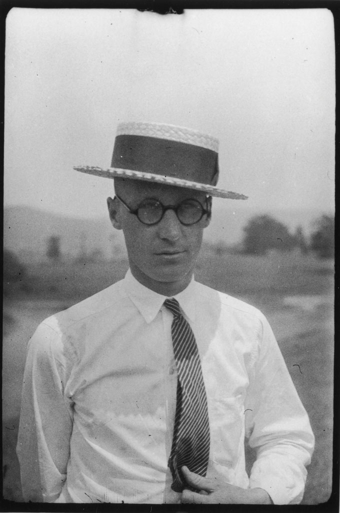Un portrait de John Scopes, vu portant un chapeau, des lunettes rondes et une cravate.