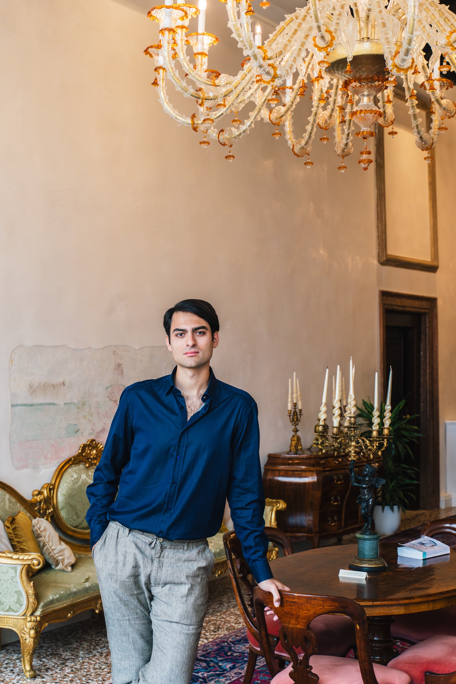 L'image peut contenir la lampe de lustre Personne adulte des vêtements debout Pantalon Pantalon Publication de chaise de chaise et table