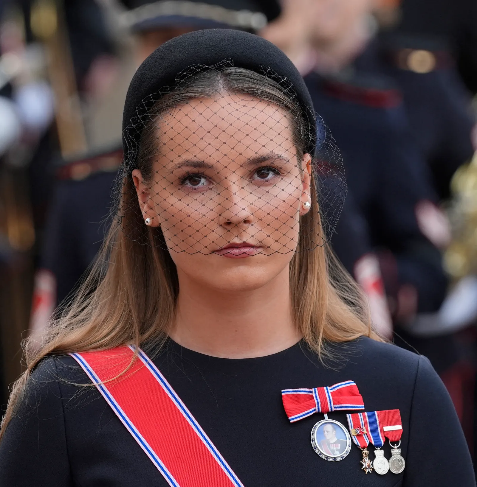 La princesse héritière Ingrid Alexandra de Norvège porte une robe noire, des insignes royaux et une ceinture rouge. Elle est aussi...