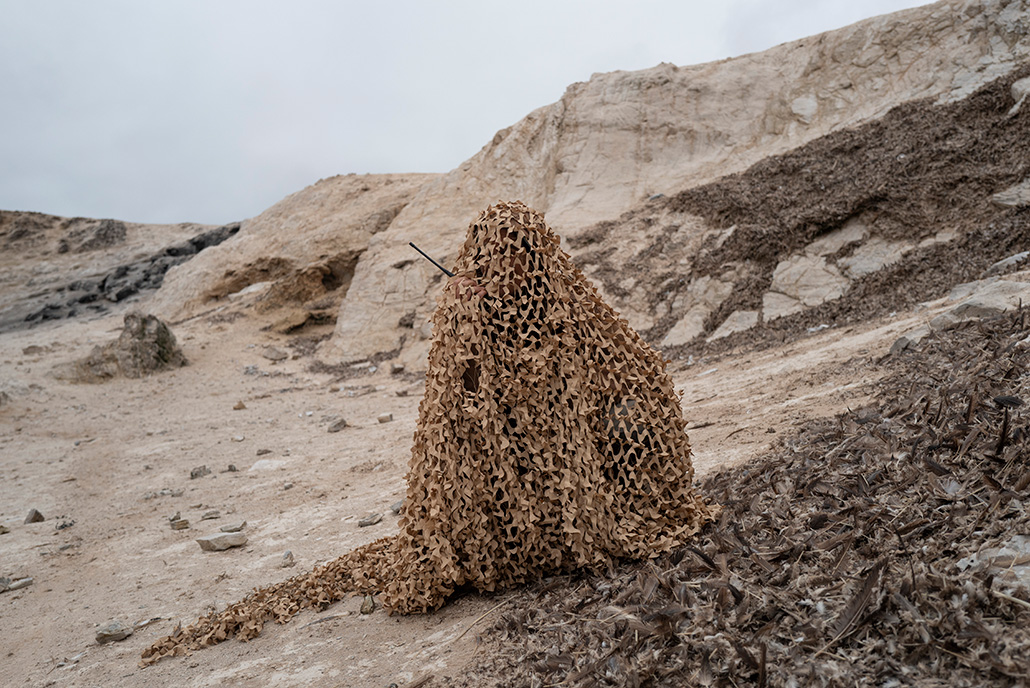 Une forme humaine recouverte d'un filet de camouflage sur un littoral