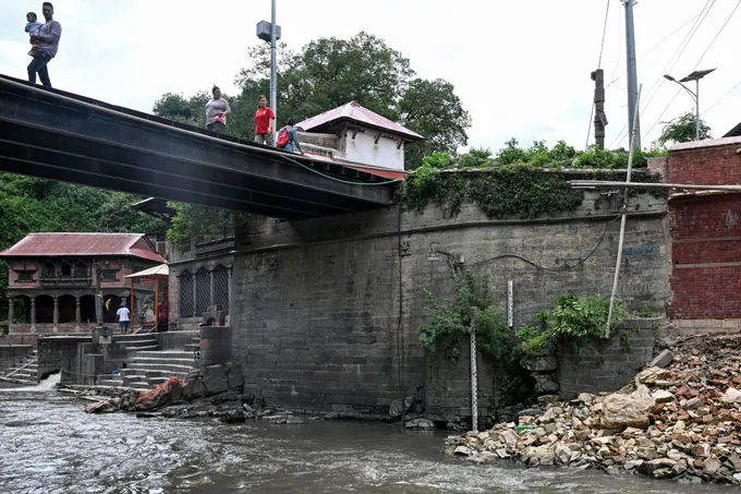Plusieurs personnes marchent sur un pont à Katmandou doté d'une sirène conçue pour avertir des inondations.
