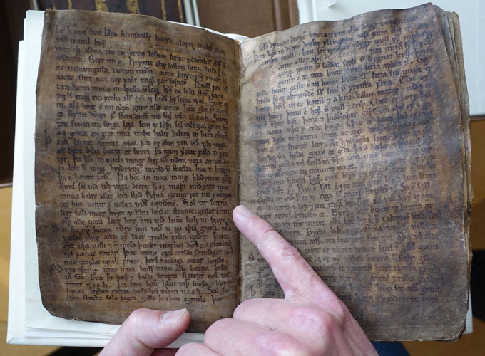 Un doigt montre l’écriture dans un vieux livre. Le texte est un poème qui fait allusion à l'impact d'une éruption volcanique sur l'atmosphère de l'Islande.
