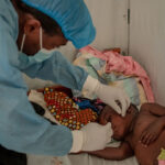 Un agent de santé portant un équipement de protection médicale vérifie un jeune garçon dans un centre de traitement mpox.