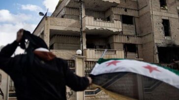 A man waves the old Syrian flag in front of the former police st, cc Flickr Freedom House, modified, https://creativecommons.org/licenses/by/2.0/