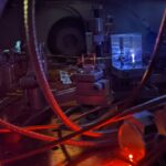 Photographie d'un équipement scientifique, notamment d'un faisceau laser éclairant un gaz à l'intérieur d'une chambre à vide.
