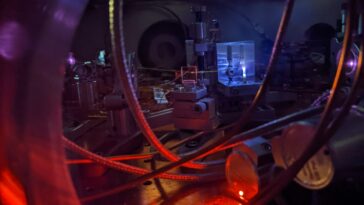 Photographie d'un équipement scientifique, notamment d'un faisceau laser éclairant un gaz à l'intérieur d'une chambre à vide.