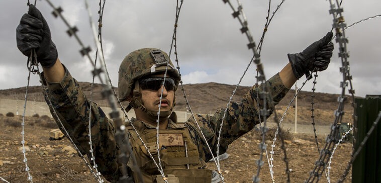 cc US Department of Defense, modified, https://flickr.com/photos/39955793@N07/45440230804/in/photolist-2cep4vf-WdexVB-gGm4hp-6ZnFgM-7biJPt-QTH5Ue-7bnhnm-WaNfG1-93eidn-NBDjfT-uoPJaw-SfpYh4-z6mvgr-7bnuQJ-ehZP6L-PK41as-93eik2-79WrQP-nQp4WW-4eAu2j-2bNC1tA-93hrk7-7a1ma3-2qbmnh1-7a1pkS-5AUzx8-35Fe3h-aeyfR9-9EbQY5-95tfCs-237UqV5-yNKiFd-68EbC1-JG9PU9-5GJRXm-6KSBK1-9xri1L-pRjuYG-c2me4h-95qcAv-c2mdMJ-JGf4Ez-KcyqdL-KcyqGm-Kcys6o-pNoMgT-2auw51X-quzxgD-6ZnDHn-quzvWz U.S. Marine Corps Lance Cpl. Victor Vargas, a combat engineer with 7th Engineer Support Battalion, Special Purpose Marine Air-Ground Task Force 7, emplaces concertina wire at the California-Mexico Border, Nov. 30, 2018. U.S. Northern Command is providing military support to the Department of Homeland Security and U.S. Customs and Border Protection to secure the Southern border of the United States. (U.S. Marine Corps photo by Lance Cpl. Brendan Mullin)