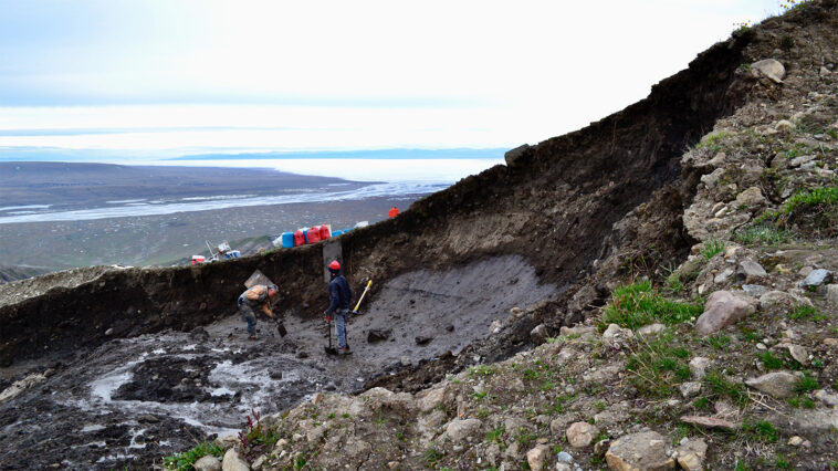 Des chercheurs sont montrés debout sur une parcelle de glace glaciaire exposée, au milieu d'un glissement de terrain.