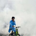 La solution de Mike Berners-Lee pour la polycrise peut être trop difficile TOPSHOT - A boy rides past as smoke billows from a burning garbage dump, in Lahore on November 1, 2024. (Photo by Arif ALI / AFP) (Photo by ARIF ALI/AFP via Getty Images)