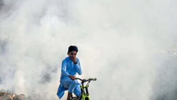 TOPSHOT - A boy rides past as smoke billows from a burning garbage dump, in Lahore on November 1, 2024. (Photo by Arif ALI / AFP) (Photo by ARIF ALI/AFP via Getty Images)