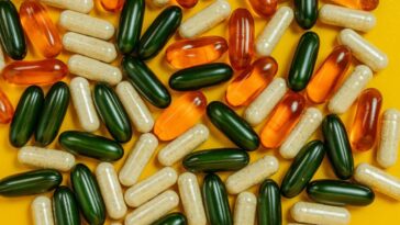 A pile of colourful supplement pills lying on a yellow table top.