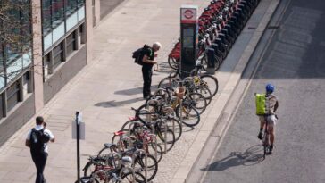 A cyclist unlocks his bike on Silk Street in the City of London, the capital