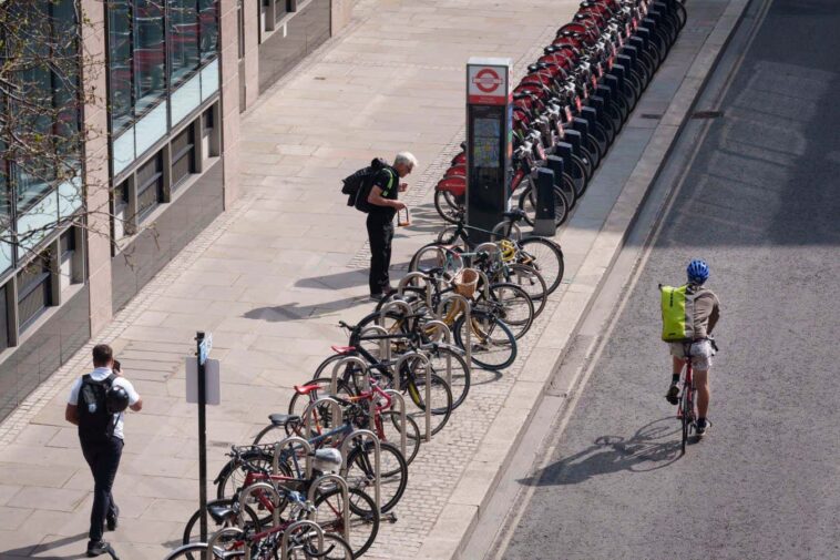 A cyclist unlocks his bike on Silk Street in the City of London, the capital