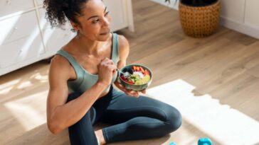 A woman eating a bowl of fruit while wearing exercise clothes