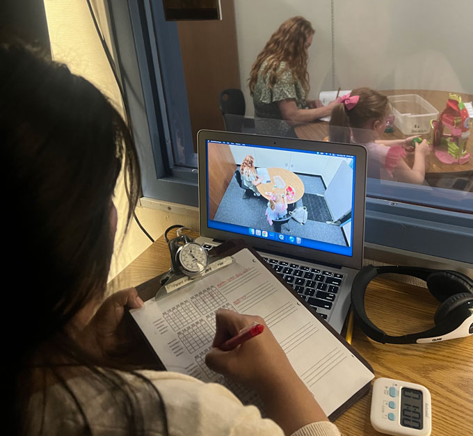 Un gestionnaire de cas observe un parent et un enfant à travers un miroir bidirectionnel lors d'une session de formation aux compétences comportementales.