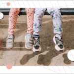 Two little girls best friends, children, sisters sit on a wooden bench in the park outdoors.