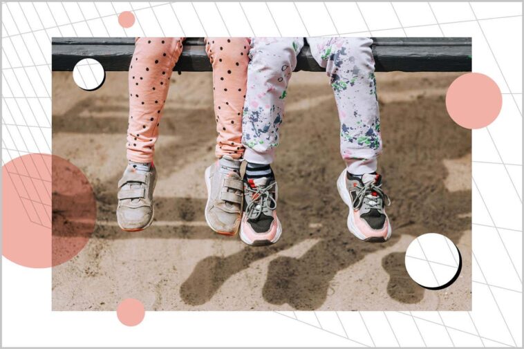 Two little girls best friends, children, sisters sit on a wooden bench in the park outdoors.