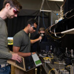 Trois hommes dans un laboratoire, un au premier plan tenant un ordinateur portable ouvert, travaillent sur un projet pour générer des nombres aléatoires.