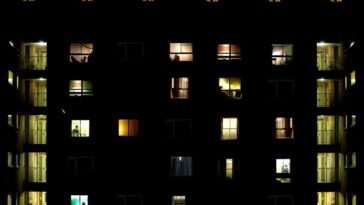 Block of flats Description Block of flats during night time with many figures in the windows and symmetrical staircase on both sides lit in green