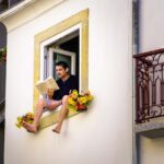 MP46X7 Man sitting on the window seal of an open window reading; man