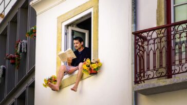 MP46X7 Man sitting on the window seal of an open window reading; man