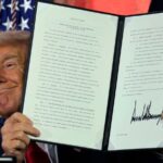 Donald Trump displays a signed executive order at an AI summit