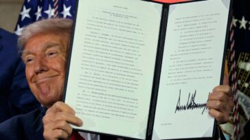 Donald Trump displays a signed executive order at an AI summit