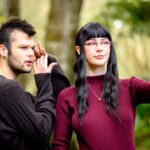 Gen z friends make a TikTok video with a cell phone. The man is a LGBTQIA person and the female is a young woman living with alopecia. University students and friends