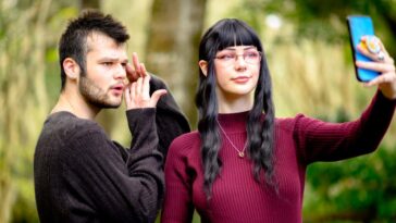 Gen z friends make a TikTok video with a cell phone. The man is a LGBTQIA person and the female is a young woman living with alopecia. University students and friends