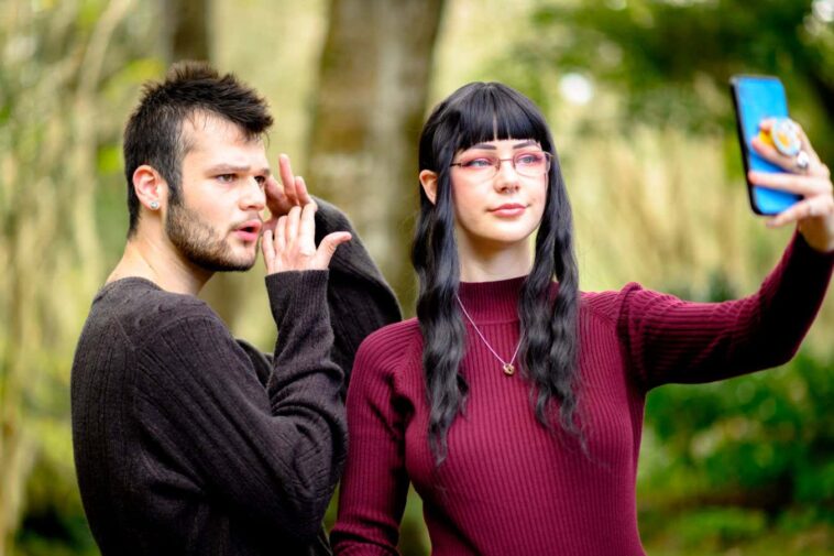 Gen z friends make a TikTok video with a cell phone. The man is a LGBTQIA person and the female is a young woman living with alopecia. University students and friends