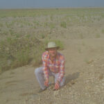 Un paysage noyé détenait des indices sur la vie des anciens parents humains Un chercheur en jean, une chemise à manches longues à carreaux et un soleil s'agenouillent sur un sol sablonneux et rocheux, tenant des outils pour rechercher le sol des fossiles.