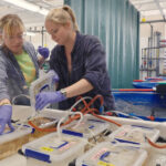 Deux chercheurs portant des gants et des blouse de laboratoire travaillent dans un laboratoire de biologie marine, examinant les conteneurs avec des couvercles étiquetés connectés par des tubes.