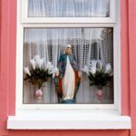 Holy Mary on window Statuette of Holy Mary and vase with plastic flowers in window on a house with bright pink walls, Irish cottage, Ireland