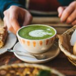 A close up of someone holding a cup of green tea with foam art