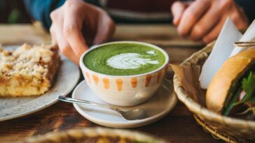 A close up of someone holding a cup of green tea with foam art