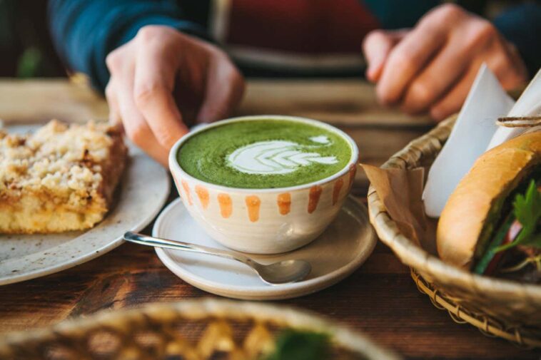 A close up of someone holding a cup of green tea with foam art