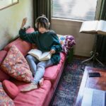 A young woman reading a book while wearing headphones.
