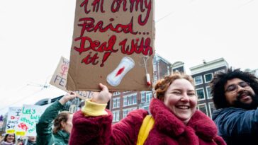 A woman is holding a placard with a sanitary towel with fake blood, during the Women
