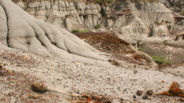 Un marteau géologique posé sur un terrain de badlands érodé avec des formations rocheuses sédimentaires en couches et un ciel nuageux en arrière-plan.