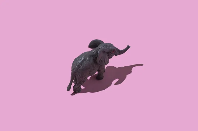 Un éléphant en jouet semble marcher sur un fond rose sur cette image prise d'en haut.