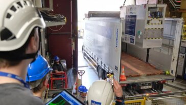 L'équipement scientifique est descendu par grue à l'arrière d'un camion, sous les yeux de personnes portant des casques de sécurité.