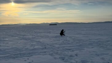 Un petit enfant construit une sculpture de glace dans un champ vide recouvert de neige