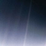 Un faible faisceau de lumière traverse un ciel sombre, avec un petit point lumineux près de son centre.
