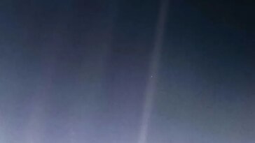Un faible faisceau de lumière traverse un ciel sombre, avec un petit point lumineux près de son centre.