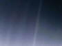 Un faible faisceau de lumière traverse un ciel sombre, avec un petit point lumineux près de son centre.