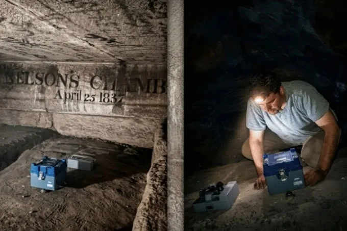 Un chercheur à l'intérieur d'une chambre sombre de la Grande Pyramide d'Égypte porte une lampe frontale et regarde une boîte bleue, avec une deuxième boîte grise à proximité - un équipement utilisé pour mesurer les vibrations à l'intérieur de la pyramide.