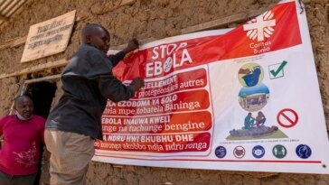 Une personne tend une grande affiche qui dit "ARRÊTEZ EBOLA" sur le côté d'un bâtiment construit en terre crue