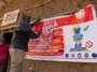 Une personne tend une grande affiche qui dit "ARRÊTEZ EBOLA" sur le côté d'un bâtiment construit en terre crue