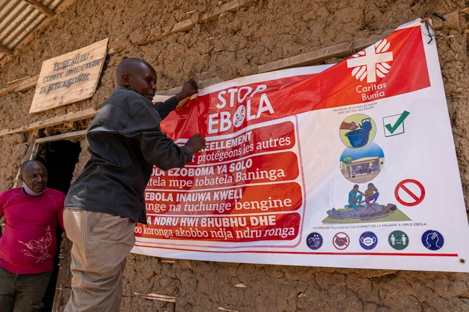 Une personne tend une grande affiche qui dit "ARRÊTEZ EBOLA" sur le côté d'un bâtiment construit en terre crue
